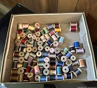 Top-down view of vintage sewing thread spools in a box showing variety of colors and wooden spools.