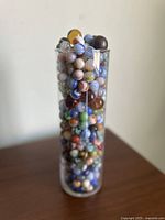 Clear cylindrical container filled with a large assortment of colorful vintage glass marbles.