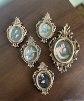 Five mini ornate gold framed classical and vintage art prints arranged on a wooden surface