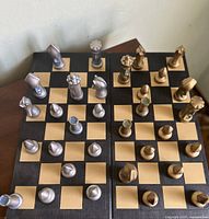 Photo showing entire chessboard with all pieces arranged for start of game. Pieces are in two metallic colors, bronze and silver tones with modern look.