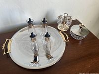 Full view of assembled set with silver-toned Lazy Susan tray holding four glass cruet bottles with black stoppers, grape cluster crystal salt and pepper shakers on a metal stand, and a covered crystal dish with metal lid.