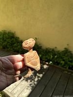 Figure of a tan-colored E.T. collectible, held in hand outdoors with greenery background.