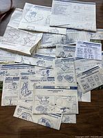Overview of various unfolded vintage G.I. Joe instruction booklets spread on a wooden surface showing multiple sheets with detailed line drawings and instructions.
