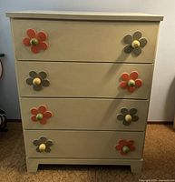 Front view of off-white dresser showing four drawers and eight flower-shaped knobs