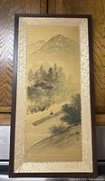 Framed vintage Japanese hanging scroll showing a mountain background, trees, house, and figure carrying wood in traditional style ink painting.