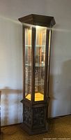 Full view of the hexagonal vintage curio cabinet showing glass panels, shelves, and carved wooden base.