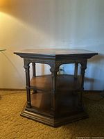 Photo of vintage hexagonal wooden end table showing front angle with carved columns and two shelves.