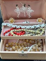 Vintage necklaces and earrings displayed in a pink jewelry box with ballerina design inside the lid.