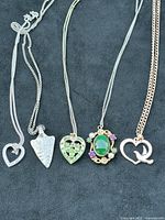 Five vintage pendants on different chains laid out on black fabric background showing details of design and materials.