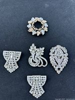 Front view of five vintage rhinestone scarf clips and one gold-tone brooch on black background