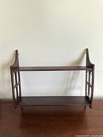 Front view of vintage wooden wall-mounted shelf showing side supports and two shelves.