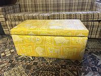 Side view of rectangular wooden chest box with yellow fabric cover featuring white and orange animal prints in patchwork style.
