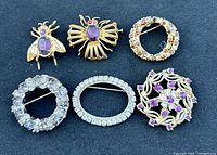 Six vintage brooches on black background showing various designs and rhinestones.