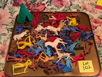 Photo shows assorted vintage plastic toy figures including cowboys, Native Americans, horses, and a green plastic teepee on a brown surface with floral background.