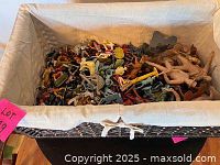 Rectangular storage basket filled with assorted vintage plastic toy soldiers and dinosaurs. Mix of green, tan, gray, red, and brown figures visible.