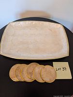 Rectangular capiz tray in cream color with gold trim alongside six matching round capiz coasters.