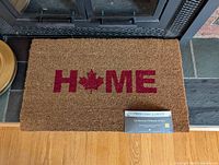 Top view of the rectangular coir door mat with the word HOME and a red maple leaf in place of the O.