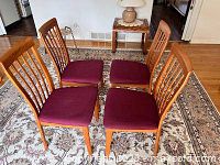 Four wooden dining chairs arranged on a patterned rug, showing wood and fabric seats