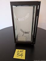 Front view of metal-framed candle lantern with frosted glass pane etched with a dragonfly design.