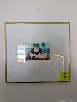 Framed etching artwork with visible gold frame, white matting, and part of the wall and reflections captured.