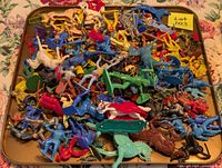 Tray filled with assorted colorful plastic toy figures including dinosaurs, animals, and human forms.
