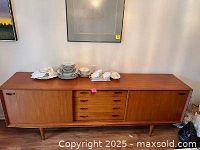 Front view of teak buffet showing four center drawers and sliding doors on each side with dishes on top