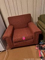 Photo of a mid-century style upholstered armchair in rust-colored fabric, showing its overall shape and condition.