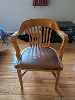 Front view of oak and leather armchair showing curved backrest and leather seat under natural light.