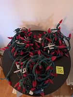 Three coiled strands of outdoor green wire Christmas lights with red LED bulbs, placed on a black round surface.