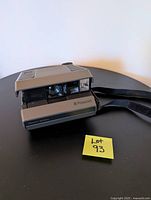 Polaroid Spectra CameraWorks instant camera showing front with lens and flash details, placed on black table with lot number visible.