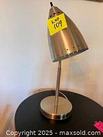Front view of retro style gooseneck desk lamp with conical brushed silver shade and round base on black surface.