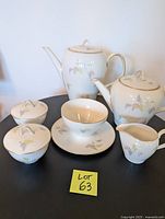 Full view of the Rosenthal coffee and tea service set arranged on a black table. Shows the coffee pot, teapot, creamer, two sugar bowls with lids, and sauce bowl with attached saucer. Each piece has a white ribbed porcelain surface with pastel leaf design and gold trim.