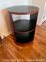 Front view of drum table showing black top, mid-tone woodgrain sides and open interior shelf