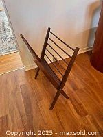 Angled side view of teakwood magazine rack showing slanted wooden sides and metal rod supports.