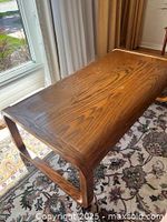 Coffee table view showing woodgrain top and one side with curved legs, in natural light on floral rug.