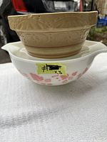 Three stacked mixing bowls shown: beige vintage mixing bowl on top with visible minor chips; two Pyrex bowls underneath with turquoise and pink patterns.