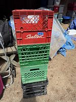 Stacked four plastic crates including a red Sealtest milk crate on top, two green milk crates below, and a black crate on bottom, showing size and color.