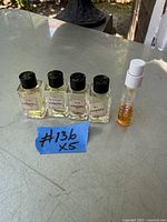 Five small perfume bottles: four square glass Chanel perfume bottles with black caps and one smaller plastic sample spray bottle with white spray cap.