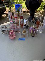 Photo showing a lot of assorted ladies perfume bottles arranged on a flat surface outdoors. Includes various shapes and sizes, some partially used, one empty pink bottle.