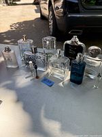 Multiple men's cologne bottles displayed on a surface outdoors including Infinity, Jaguar, Cool Water, Pleasures, CK, and small vials