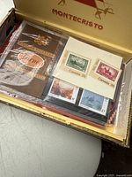 Open Montecristo cigar box showing assortment of vintage new and used stamps in protective sleeves.