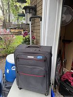 Front angled view showing the black suitcase with red trim, Air Canada branding, two zippered front pockets, telescoping handle extended, and four wheels at base.