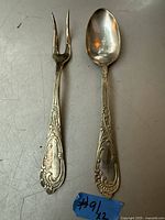 Photo showing the antique silver serving fork and spoon side by side on a flat surface with identification sticker #91/2.