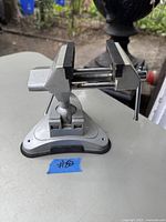 Metal bench vice with adjustable jaws and suction cup base on flat surface, front angle view showing main screw and jaw opening.
