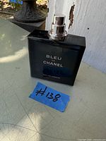 Photo of a full Bleu de Chanel Eau de Parfum bottle for men, 1.7 FL.OZ., dark blue glass bottle with silver spray nozzle. Blue tape with handwritten #138 placed in front of bottle.