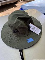 Olive green cotton bucket hat with wide brim and chin strap, Quiksilver logo, with attached tags.