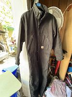 Full front view of the black Carhartt insulated coverall hanging, showing overall condition and shape.