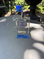 Photo of a full 3.4 FL.OZ. bottle of Chanel No. 5 L'Eau perfume spray without cap, displayed outdoors on a table with a garden background.