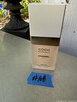 Front view of full 12 fl oz Coco Mademoiselle Chanel hair mist parfum bottle with white and gold cap and label, placed on outdoor surface with lot number #168 indicated.