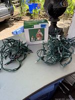 Department 56 Christmas Market The Gingerbread Booth box and two bundles of green wire Christmas lights on a table outdoors.